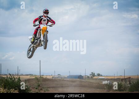 Un homme caucasien dans un casque de motocross jaune vif, à cheval sur un vélo de terre jaune et blanc, sautant en plein air sur une piste de terre Banque D'Images
