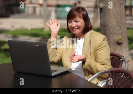 Femme d'affaires adulte élégante, freelance, mentor parle avec un smartphone et parcourt un ordinateur portable au café City Street. Concept de travail à distance, leadership, Banque D'Images