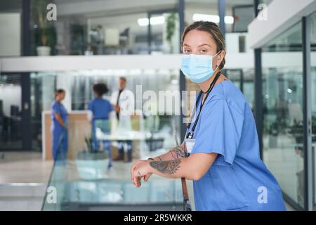 Messagerie instantanée toujours en communication. Portrait court d'une jeune infirmière attirante portant un masque facial et debout dans la clinique. Banque D'Images