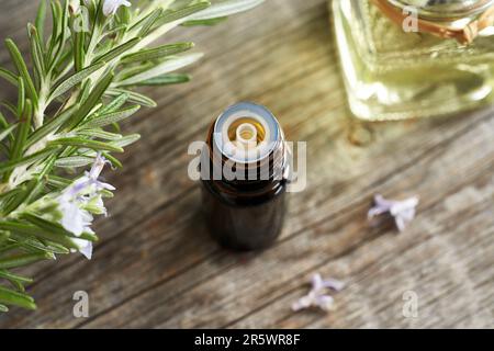 Bouteille d'huile essentielle avec brindilles de romarin frais en fleurs Banque D'Images