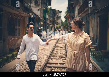 Laissez l'amour montrer la voie. Un jeune couple marchant sur les voies ferrées à travers les rues du Vietnam. Banque D'Images