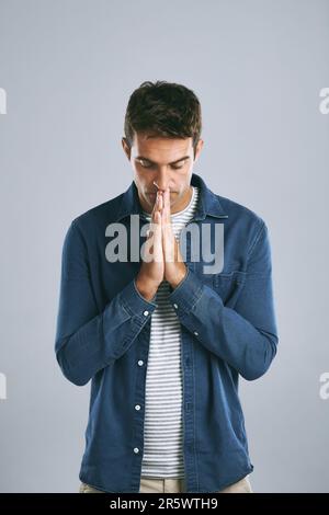 J'espère et je prie... un bel homme qui regarde anxieux sur fond gris. Banque D'Images