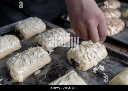 Un jeune hispanique couvre un petit pain rempli de chocolat avec des garnitures d'amande avant du cuire sur un plateau Concept de pain sucré mexicain traditionnel Banque D'Images