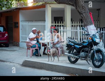 Barranquilla, Atlantico, Colombie - 17 février 2023: Trois hommes assis parlant sur une table en plastique dans la rue avec leur chien et leur moto Banque D'Images