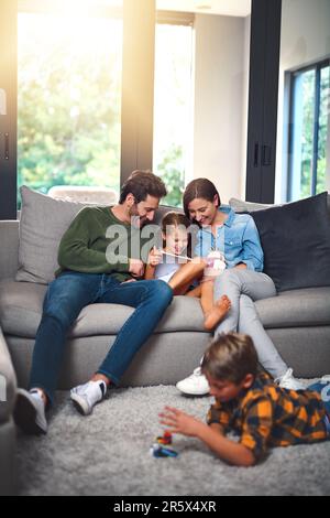 Collage et navigation. une mère, un père et leur fille utilisant une tablette ensemble sur le canapé tandis que leur fils joue sur le sol dans le salon à Banque D'Images