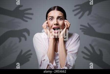 Illusion paranoïaque. Femme effrayée criant sur fond gris. Des ombres de mains atteignant pour elle symbolisant la peur et l'anxiété Banque D'Images