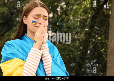 Jeune femme ukrainienne émotive avec des mains clashed dehors, espace pour le texte Banque D'Images