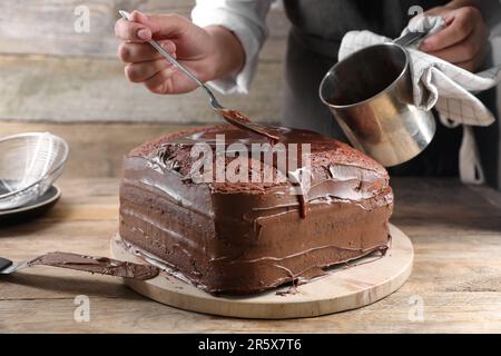 Femme versant de la crème au chocolat dans un gâteau maison de Savoie à table en bois, gros plan Banque D'Images