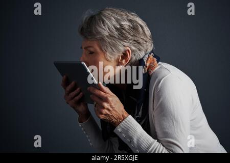 C'est une technologie incroyable. Photo studio d'une femme âgée gaie debout et donnant à sa tablette un baiser. Banque D'Images