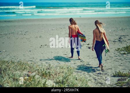 C'est là que le temps est resté immobile. un jeune couple qui marche sur la plage avec leurs planches de surf. Banque D'Images