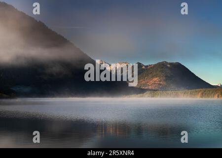 Le brouillard laisse place au soleil au lever du soleil d'automne à Sylvensteinsee, Bavière, Allemagne Banque D'Images