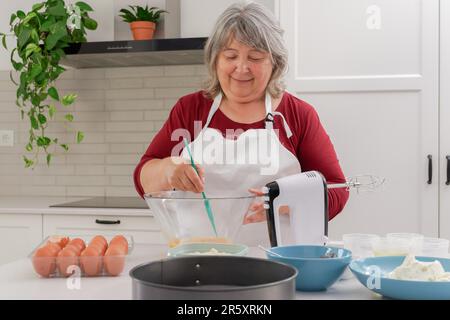 Les femelles cuisent sur un tablier blanc en battant les œufs dans un bol avec une spatule Banque D'Images