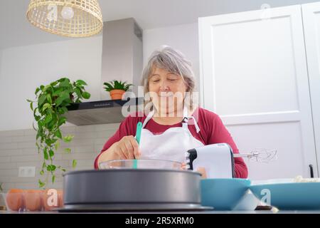 Les femelles cuisent sur un tablier blanc en battant les œufs dans un bol avec une spatule Banque D'Images