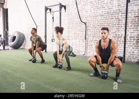 Nous nous motivons mutuellement à continuer. un groupe de fitness tenant des kettlebells tout en faisant des squats à la salle de gym. Banque D'Images