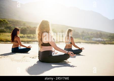 Effacez votre esprit. trois jeunes femmes pratiquant le yoga sur la plage. Banque D'Images