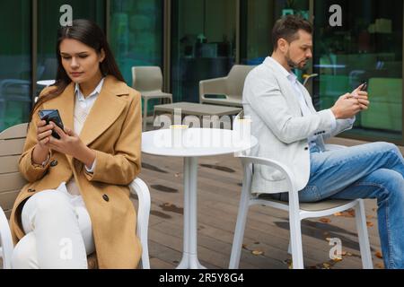 Contrarié de se disputer en couple avec des téléphones intelligents dans un café en plein air. Problèmes de relation Banque D'Images