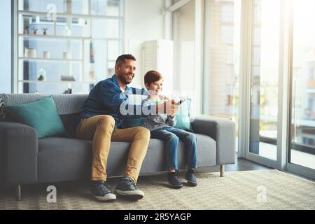 Changement de chaîne. un petit garçon joyeux et son père regardant la télévision ensemble tout en étant assis sur le canapé à la maison. Banque D'Images