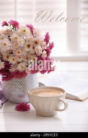 Carte de bienvenue. Tasse de café frais, livre ouvert et beau bouquet sur table en bois blanc près de la fenêtre Banque D'Images