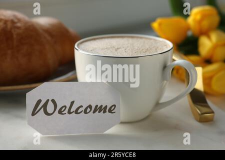 Carte de bienvenue, tasse de café aromatique et croissant sur plateau et superbes tulipes jaunes Banque D'Images