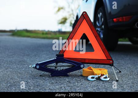 Triangle d'avertissement d'urgence, sangle de remorquage et cric articulé près de la voiture à l'extérieur. Équipement de sécurité Banque D'Images