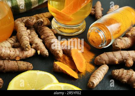 Racines turmériques, poudre, citron tranché et tasse de thé savoureux sur table noire texturée, en gros plan Banque D'Images