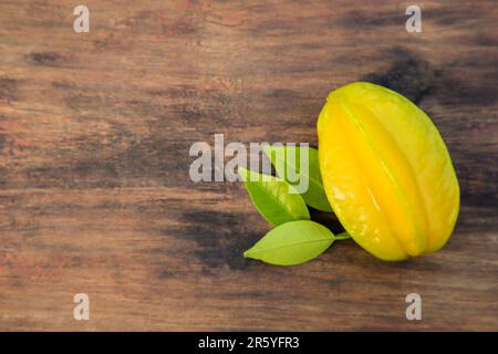 Une délicieuse carambola mûre avec des feuilles sur une table en bois, vue sur le dessus. Espace pour le texte Banque D'Images