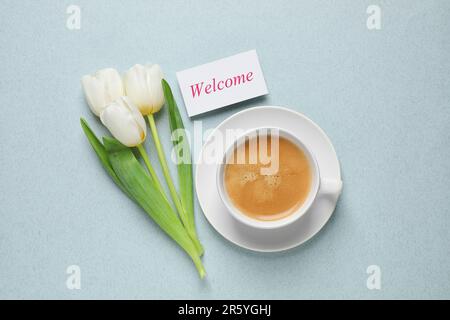 Carte de bienvenue, superbes tulipes blanches et tasse de café aromatique sur fond bleu clair pâle, plat Banque D'Images