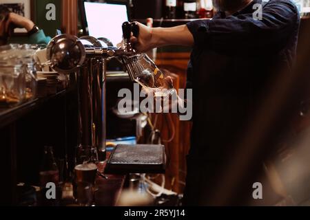 le barman verse de la bière brune à la pression dans le pub derrière le bar Banque D'Images