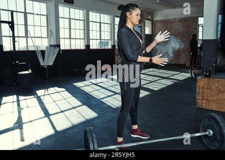 Se préparer à lever des poids. une jeune femme se laçant les mains avec de la craie avant de soulever des poids. Banque D'Images