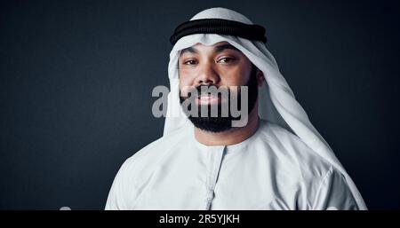 Il se sent mieux en portant ses vêtements traditionnels. Photo en studio d'un jeune homme vêtu de vêtements traditionnels islamiques se posant contre une obscurité Banque D'Images