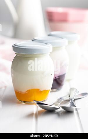 Yaourt blanc et fruité en pot sur la table blanche. Banque D'Images