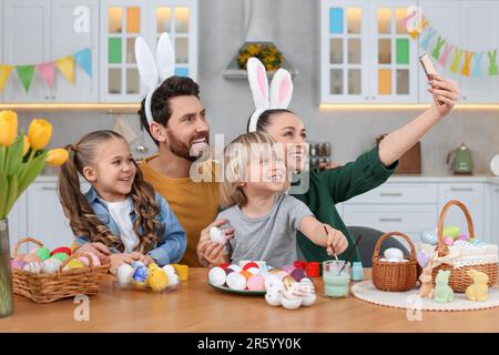 Famille faisant le selfie tout en peignant des oeufs de Pâques à la table dans la cuisine Banque D'Images