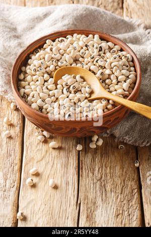 Gros plan de pois ou de haricots à yeux noirs crus dans un bol sur une table en bois. Verticale Banque D'Images