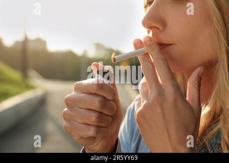 Jeune femme éclairant la cigarette à l'extérieur, gros plan des mains Banque D'Images
