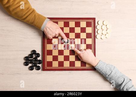 Homme senior jouant aux dames avec une femme à une table en bois blanc, vue de dessus Banque D'Images