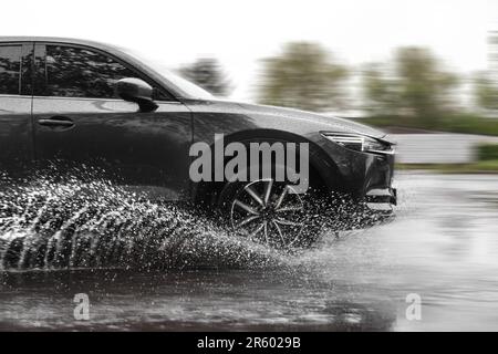 Voiture noire traversant la flaque à grande vitesse le jour de la pluie, effet de flou de mouvement Banque D'Images