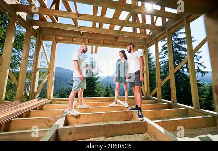 Homme avec plan de vitrines pour couple le processus de construction de la maison encadrée en bois. Les investisseurs inspectent leur futur logement dans les montagnes près de la forêt. Concept de construction écologique contemporaine. Banque D'Images