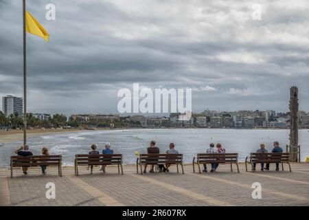 Cinq couples assis sur cinq bancs sur la promenade du port de plaisance et donnant sur la plage Levante de la mer Méditerranée à Salou, Tarragone, Espagne. Banque D'Images