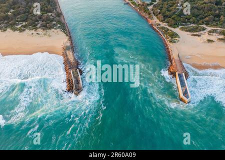 Vue aérienne de l'eau qui se déforme dans l'intérieur des terres à travers les murs du brise-lames avec plage de chaque côté à l'entrée du lac à Gippsland, Victoria, Australie. Banque D'Images