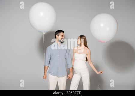 Positif et tendance s'attendant à des parents tenant les mains et ballons de fête pendant la fête et le sexe révéler la fête surprise sur fond gris, la Folasi Banque D'Images