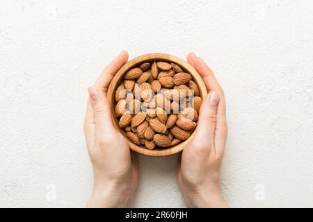 Femme mains tenant un bol en bois avec des noix d'amande. Aliments sains et en-cas. En-cas végétariens de différentes noix. Banque D'Images