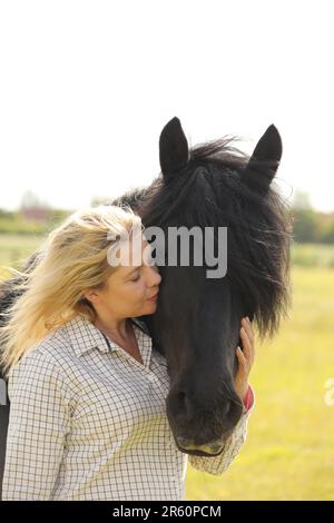 Une femme blonde embrasse un poney noir tombé Banque D'Images