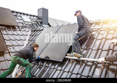 Ouvriers installant des panneaux solaires sur le toit d'une maison Banque D'Images