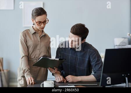 Portrait de deux jeunes professionnels regardant le presse-papiers tout en examinant le projet INFORMATIQUE au bureau, espace de copie Banque D'Images