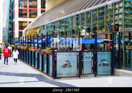 Toronto, Canada - 13 mai 2023 : un homme et une femme qui descendent un passage pavé le long d'une zone clôturée avec des parasols à baldaquin bleu où les gens se trouvent Banque D'Images