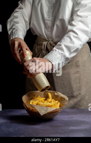 Un gros plan d'une personne saupoudrant du sel sur un panier de frites Banque D'Images