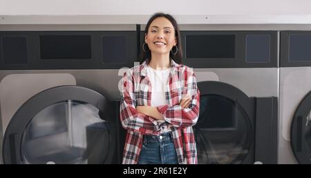 Bonne jeune femme posant près des lave-linge à la blanchisserie publique Banque D'Images