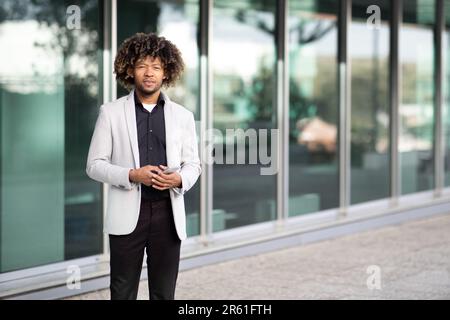 Homme d'affaires afro-américain d'âge moyen debout près d'un immeuble de bureaux, tenant le téléphone, regardant l'appareil photo, l'espace de copie Banque D'Images