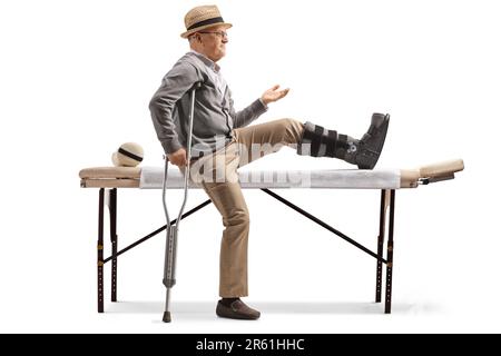 Homme âgé avec un étrésillon de jambe assis sur un lit pour la physiothérapie isolé sur fond blanc Banque D'Images