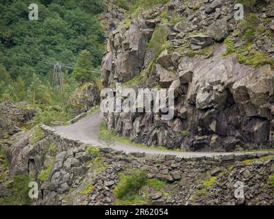 Une voiture d'époque navigue sur une route entourée de terrains rocheux et de montagnes majestueuses en arrière-plan Banque D'Images